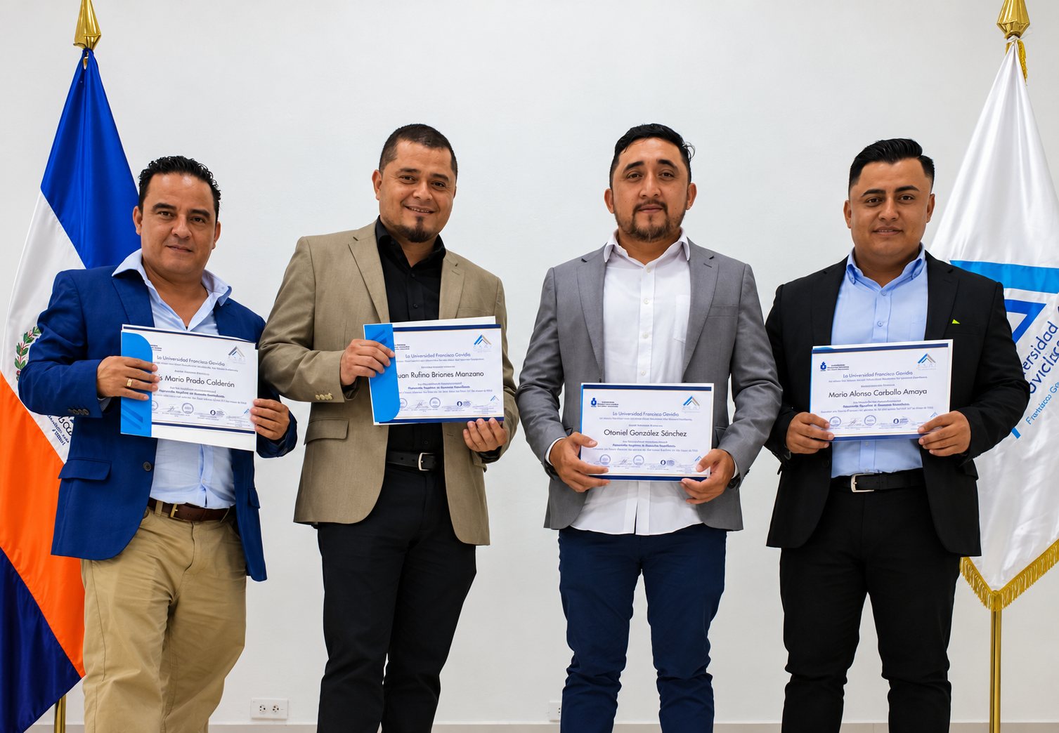 Cuatro graduados mostrando sus diplomas junto a banderas