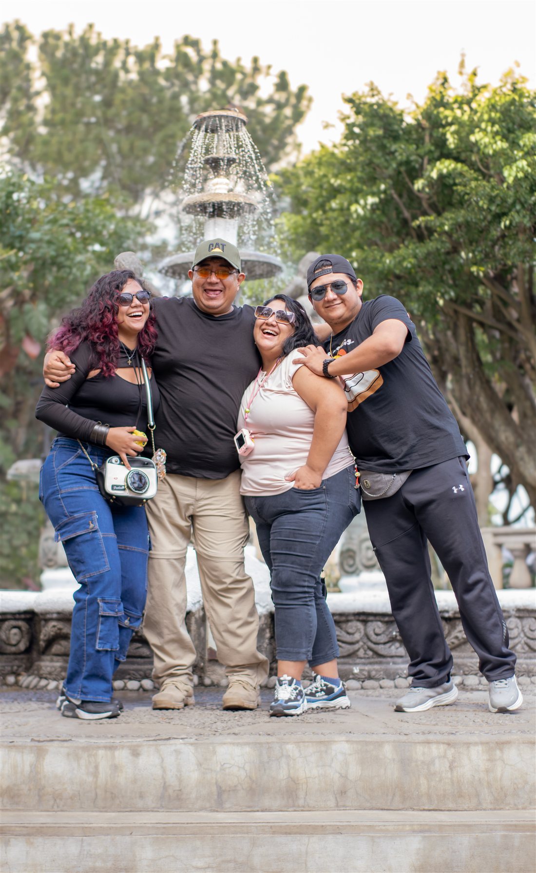 Cuatro personas abrazadas y riendo frente a una fuente
